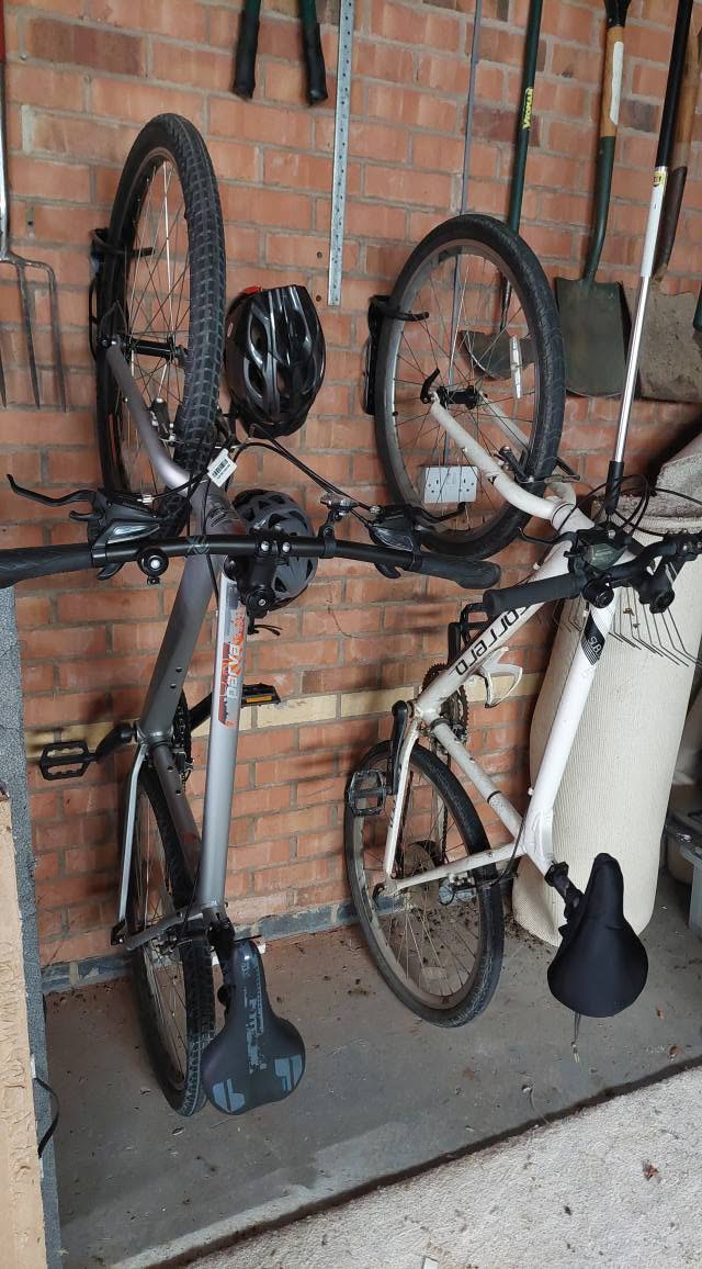 Two bikes hung on wall hooks in a garage