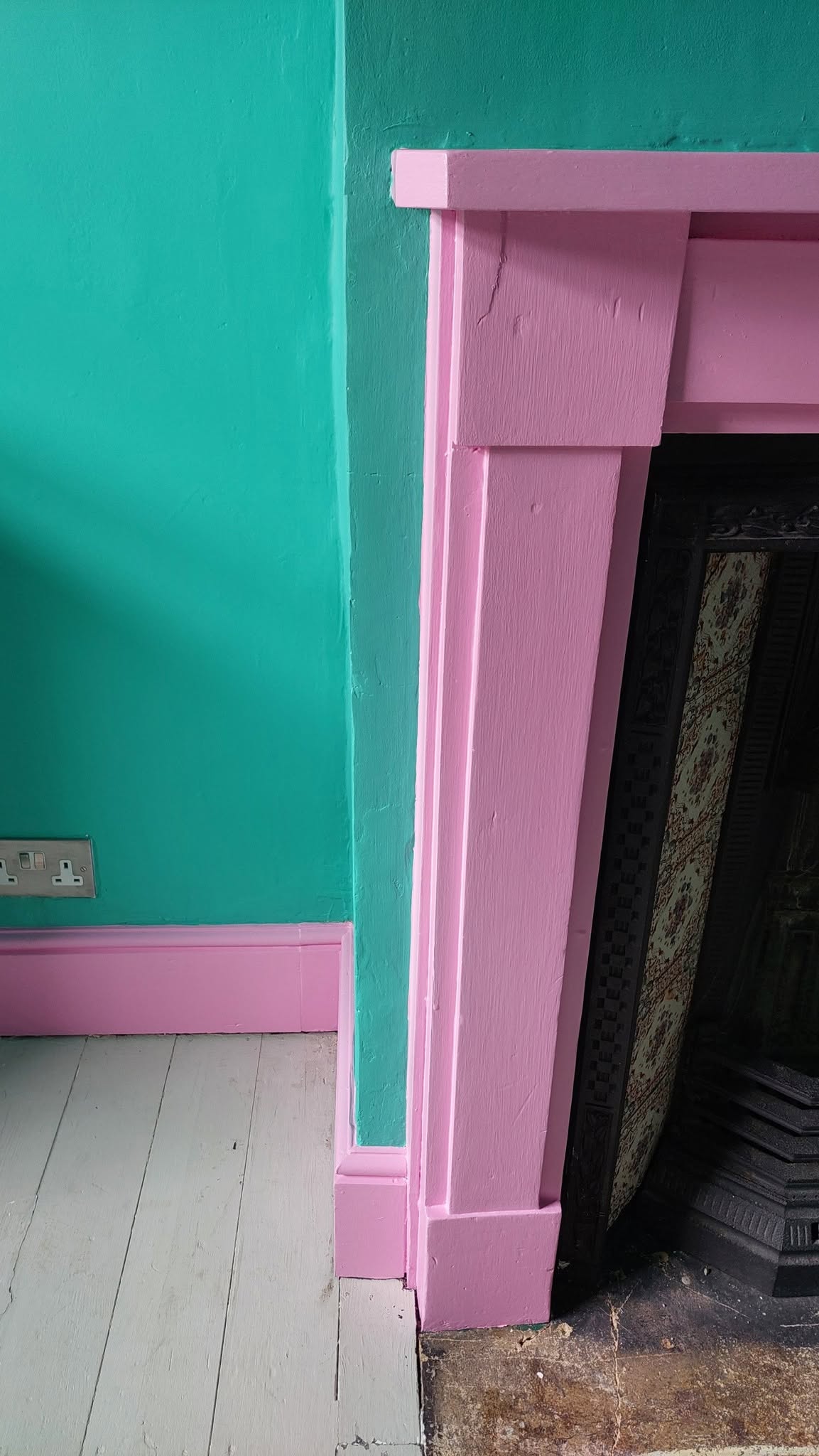 Pink fireplace surround and skirting against a teal wall
