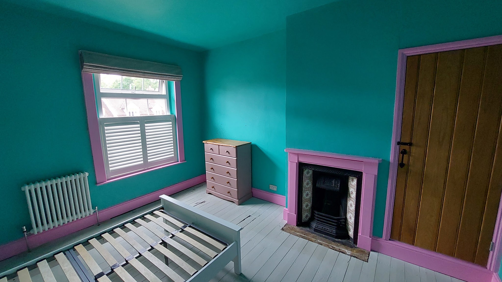 Bedroom with teal walls, pink skirting and fireplace, and painted floorboards